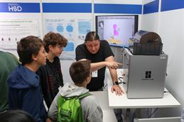 Ein HSD-Mitarbeiter erklärt drei jungen Besuchern einen 3D-Drucker am Messestand der Hochschule bei der Nacht der Wissenschaft in Düsseldorf.